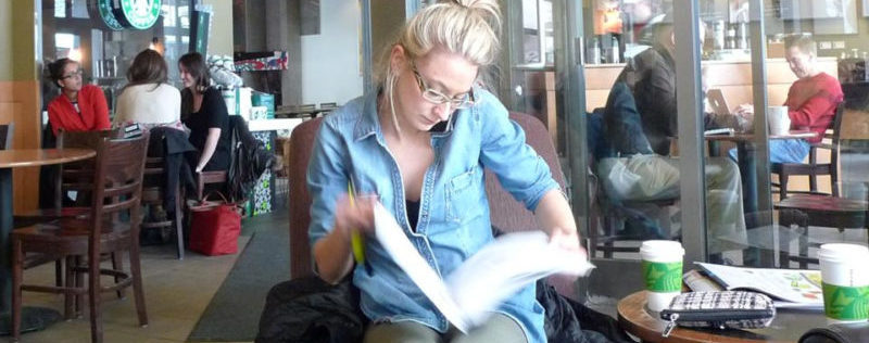 Woman sitting on a chair in a Starbucks coffee shop looking through a binder of pages while talking on the phone